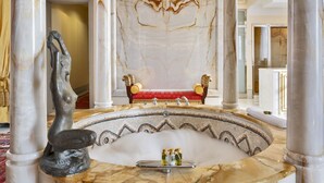 Une salle de bain luxueuse avec un lavabo en marbre, un banc rouge et un grand miroir.
