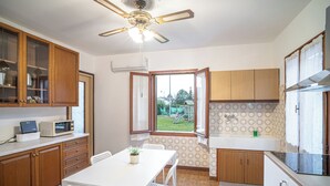 A kitchen with wooden cabinets, a white table, and a ceiling fan. - La Casetta di Roveredo, independent house. Near the Dolomites and Aviano Base (Roveredo in Piano)