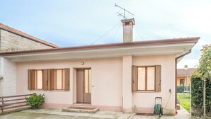 A two-story house with a flat roof, a chimney, and a garden area with a hose and a small plant. - La Casetta di Roveredo, independent house. Near the Dolomites and Aviano Base (Roveredo in Piano)
