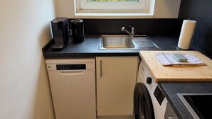 Cozinha compacta com máquina de lavar louça, máquina de lavar roupa, cafeteira e pia.