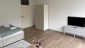 Quarto com cama, guarda-roupa, televisão e uma pequena mesa com flores.