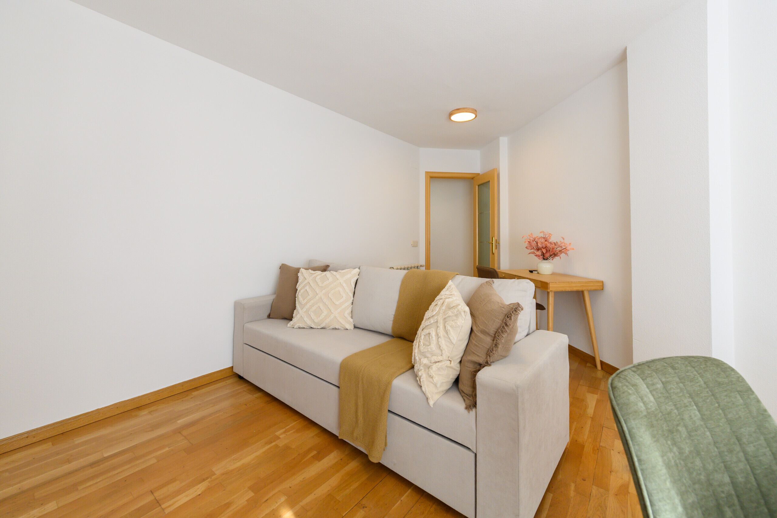 A modern living room with a sofa, a wooden floor, and a small table with a vase.