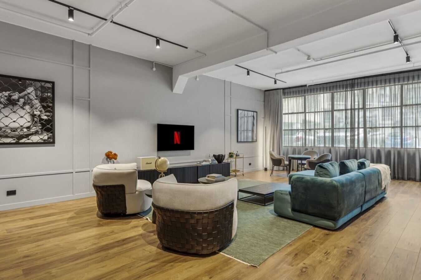 A modern living room with a flat-screen TV, a sofa, a coffee table, and a dining area with a table and chairs.