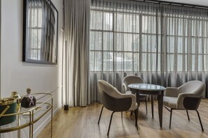 Ein Zimmer mit rundem Glastisch, vier Stühlen, einem goldrahmen Seitentisch mit Flaschen und einem großen Fenster mit transparenten Vorhängen.