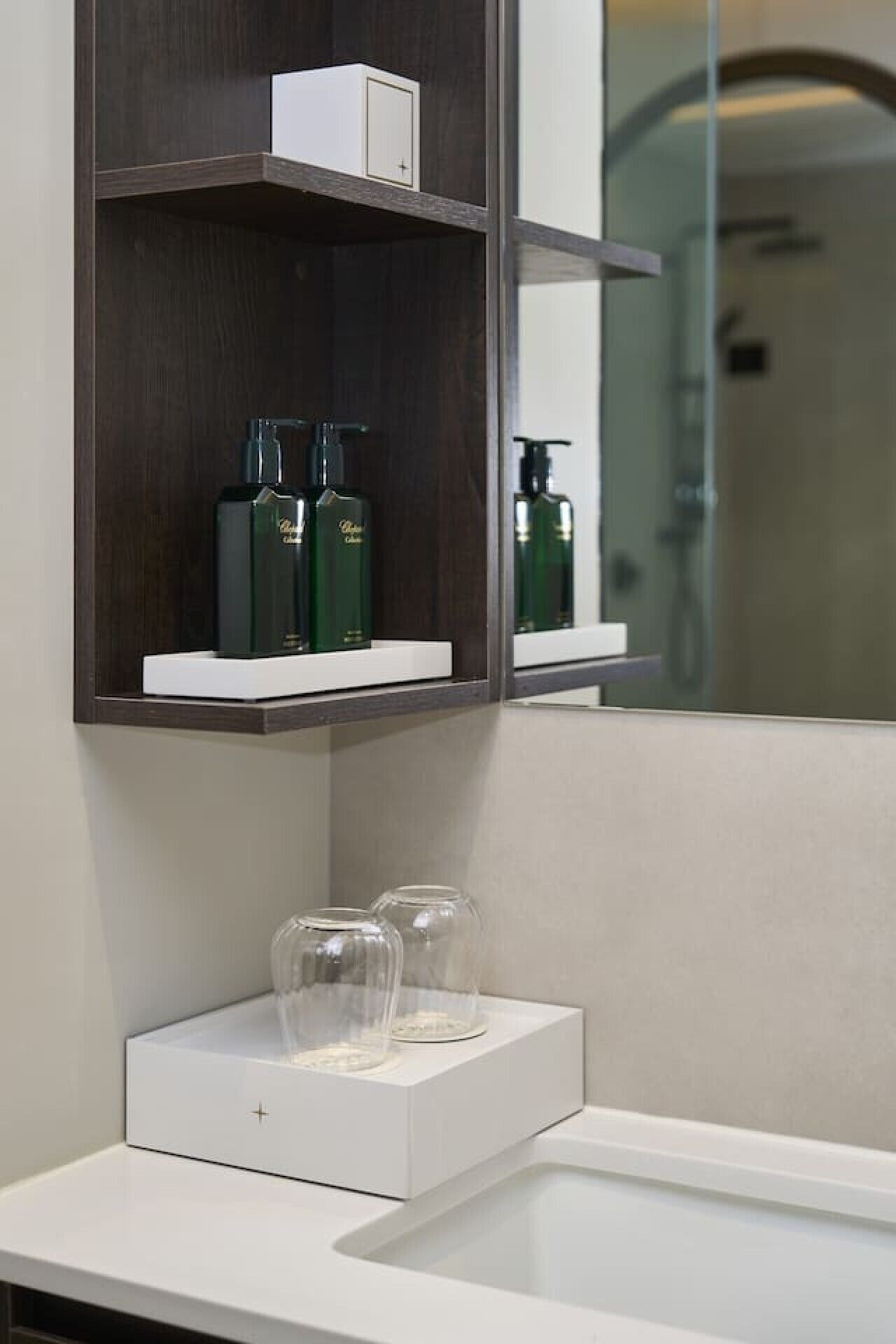 A bathroom with a white countertop, a mirror, and shelves with toiletries.