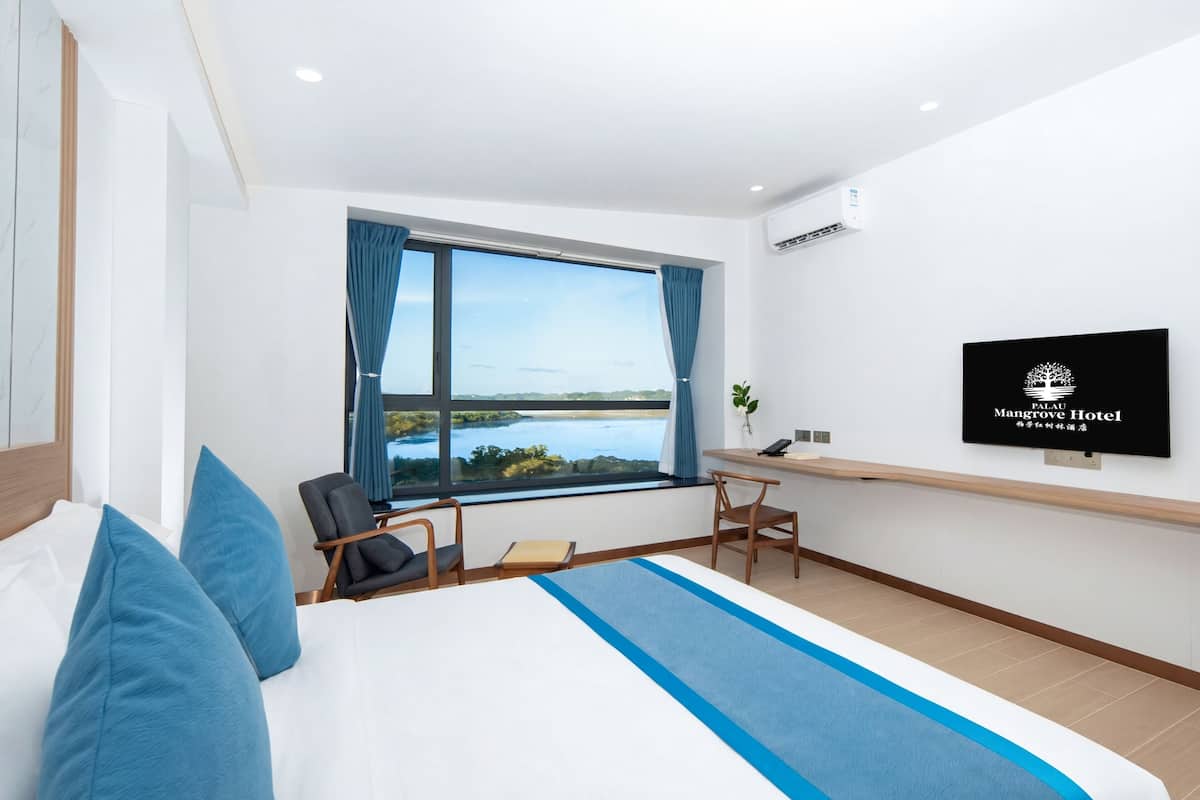 Ein Hotelzimmer mit Bett, Schreibtisch, Stuhl, Fernseher und einem Fenster mit Aussicht.