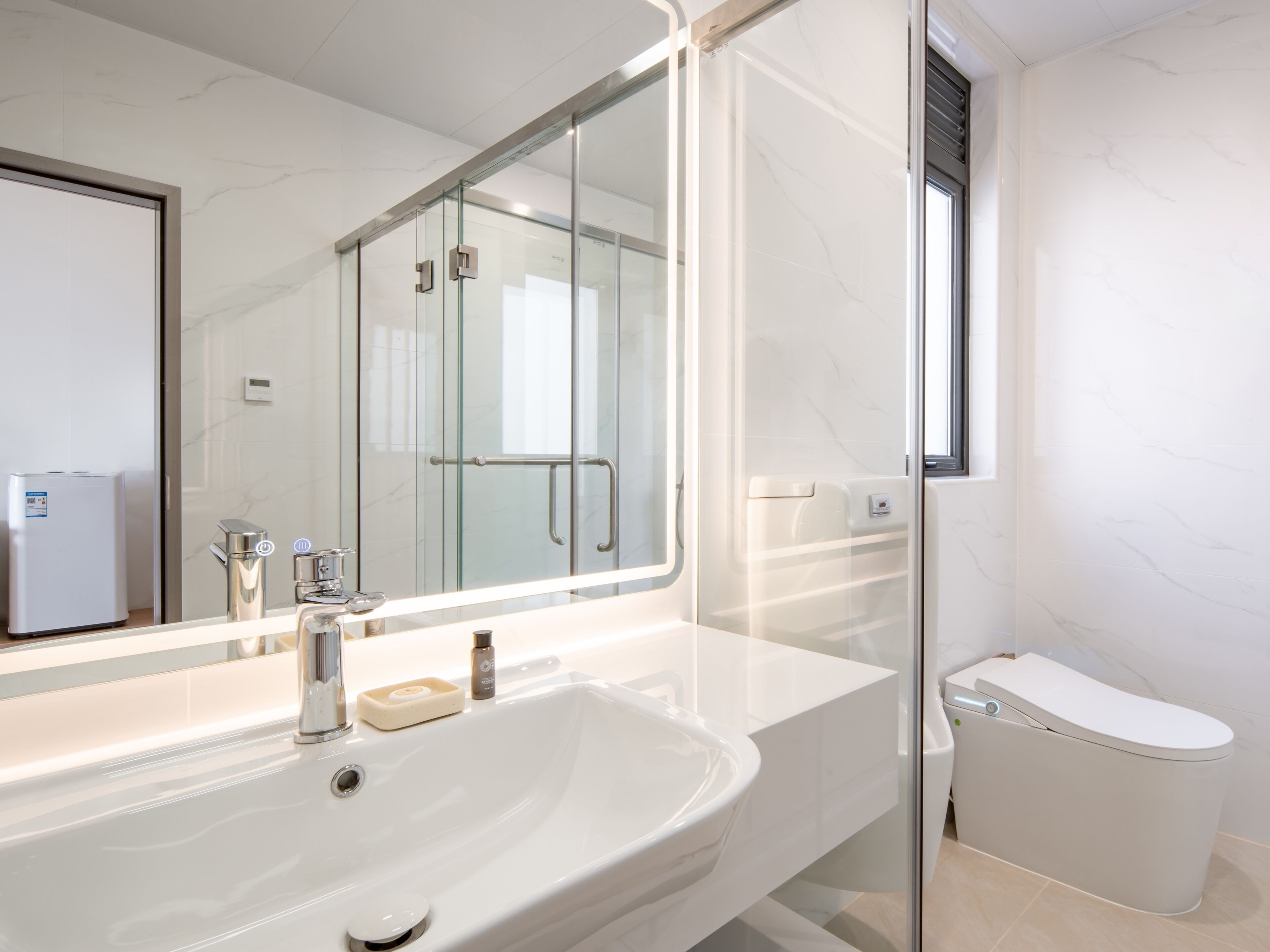 Une salle de bain moderne avec une douche à parois de verre, un lavabo blanc doté d’un porte-savon et des toilettes.