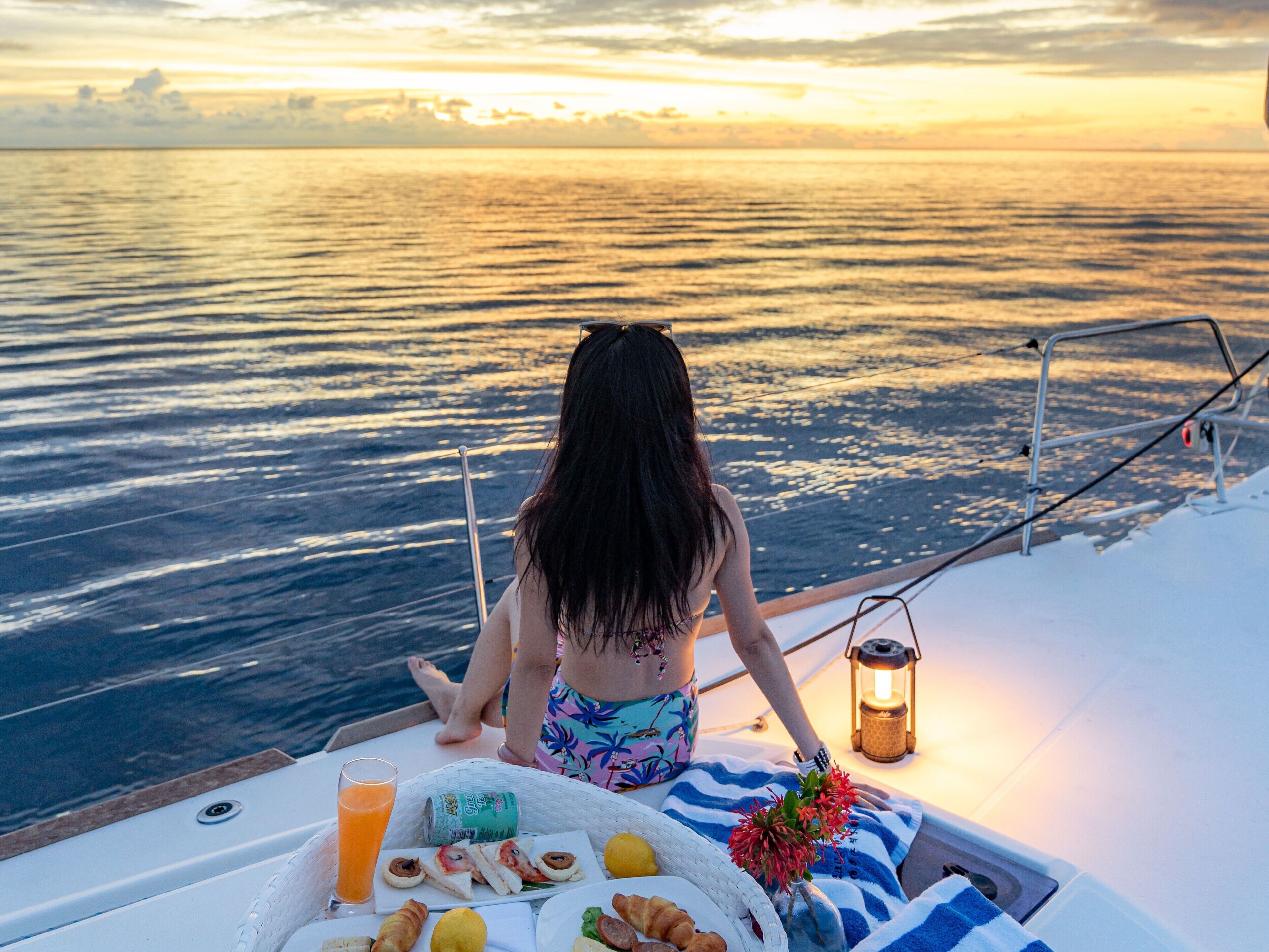 A person on a boat with a table of food and drinks, a lantern, and a view of the water.