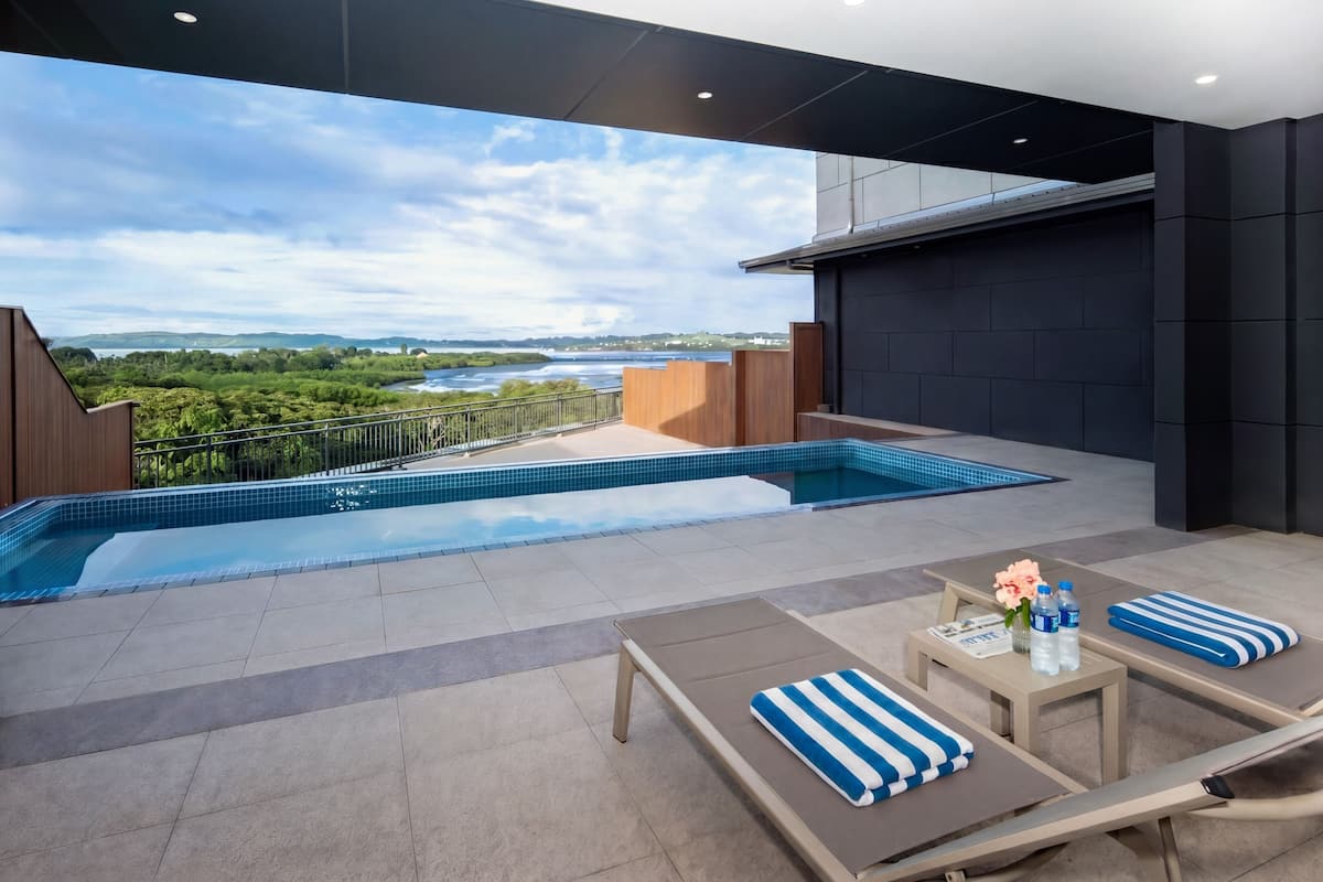 Ein Pool auf dem Dach mit Blick auf einen Fluss und Grünflächen, Liegestühle und ein Tisch mit Blumenvase.