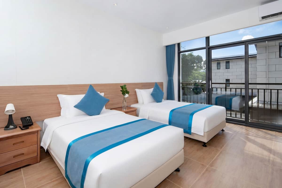 Ein Hotelzimmer mit zwei Betten, einem Nachttisch, einer Lampe, einem Telefon und Blick ins Freie.