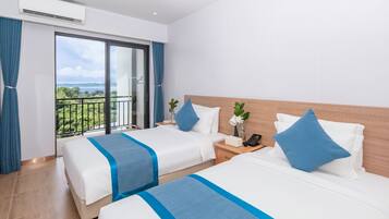 A hotel room with two beds, a balcony with a view, and a small table with a phone and a vase.