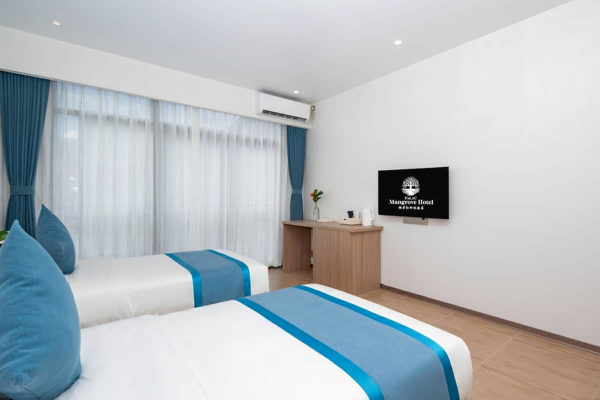 Ein Hotelzimmer mit zwei Betten, einem Schreibtisch, einem Fernseher und einem Fenster mit Vorhängen.