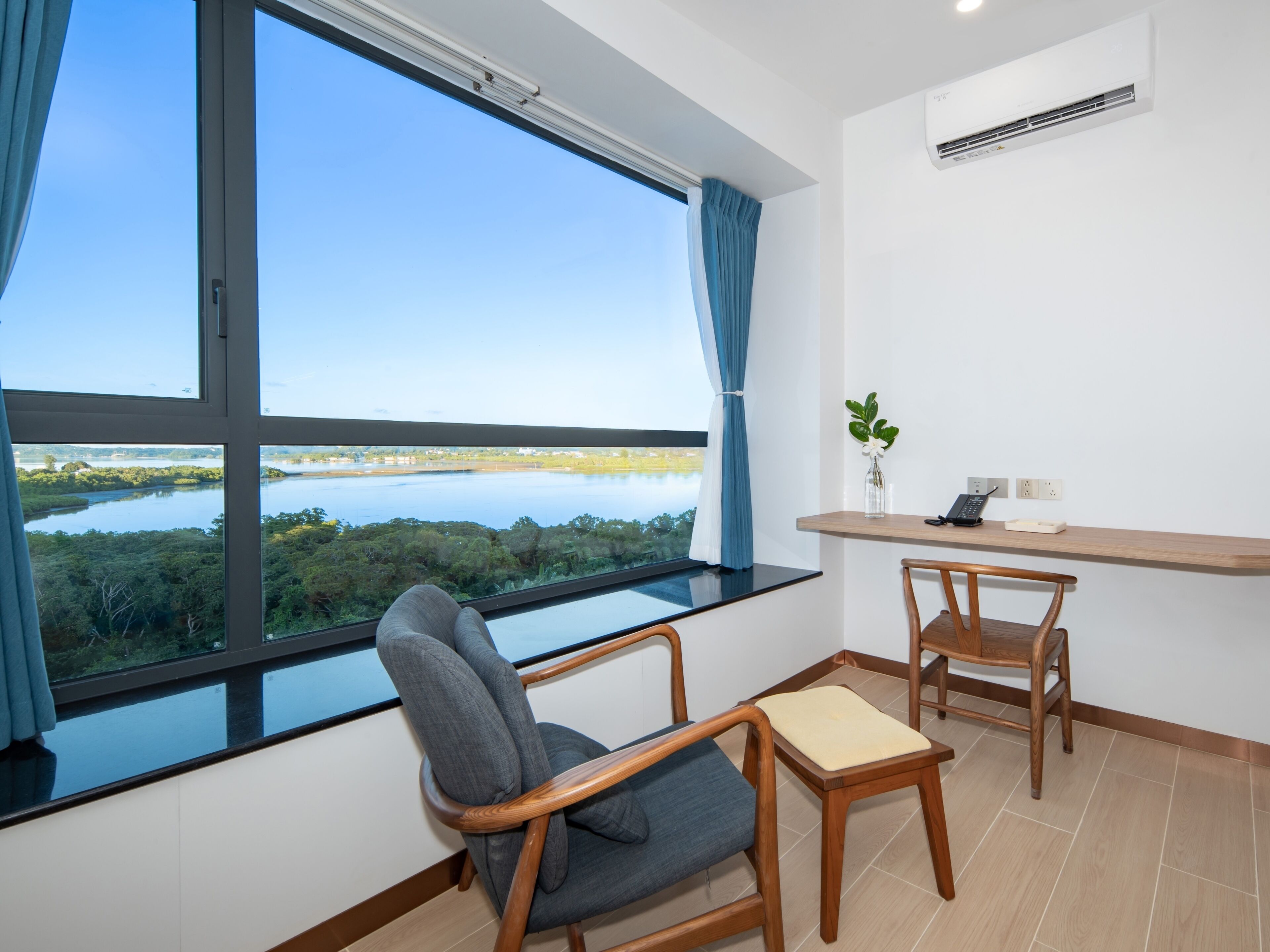 A room with a large window, a desk, two chairs, a small plant, and an air conditioning unit.