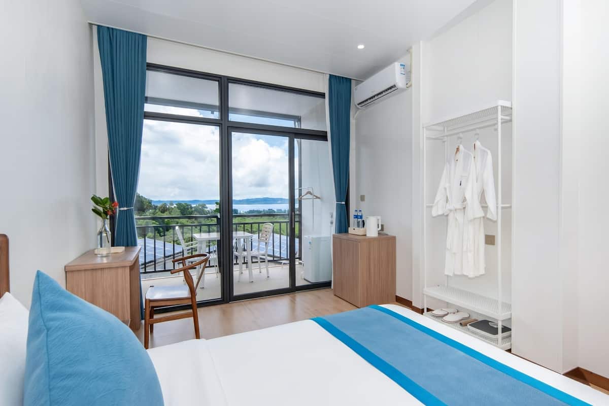 Ein Hotelzimmer mit einem großen Bett, einem Schreibtisch mit Stuhl, einem Kleiderschrank und einem Balkon mit Blick.