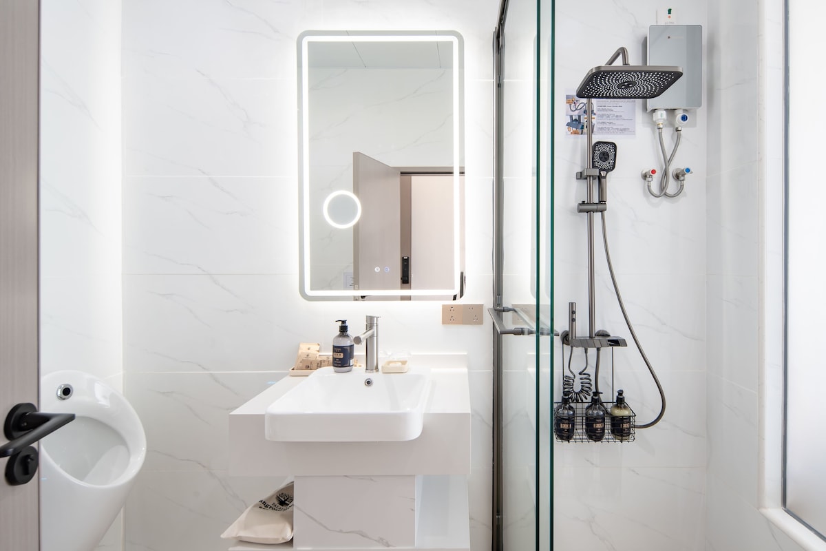 Une salle de bain moderne dotée d’une douche à parois de verre, d’un lavabo blanc et d’un miroir avec éclairage intégré.
