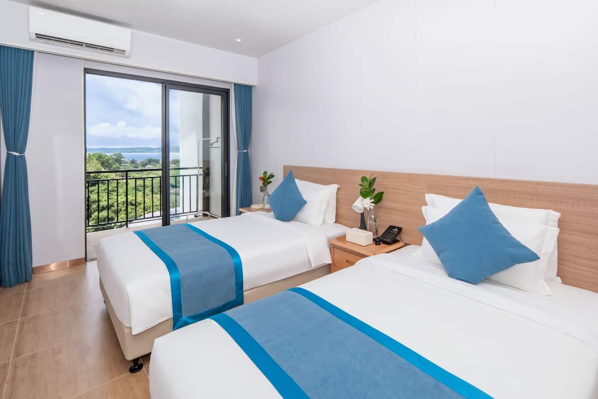 Ein Hotelzimmer mit zwei Betten, einem Balkon und Blick sowie einem kleinen Tisch mit Telefon und Blumenvase.