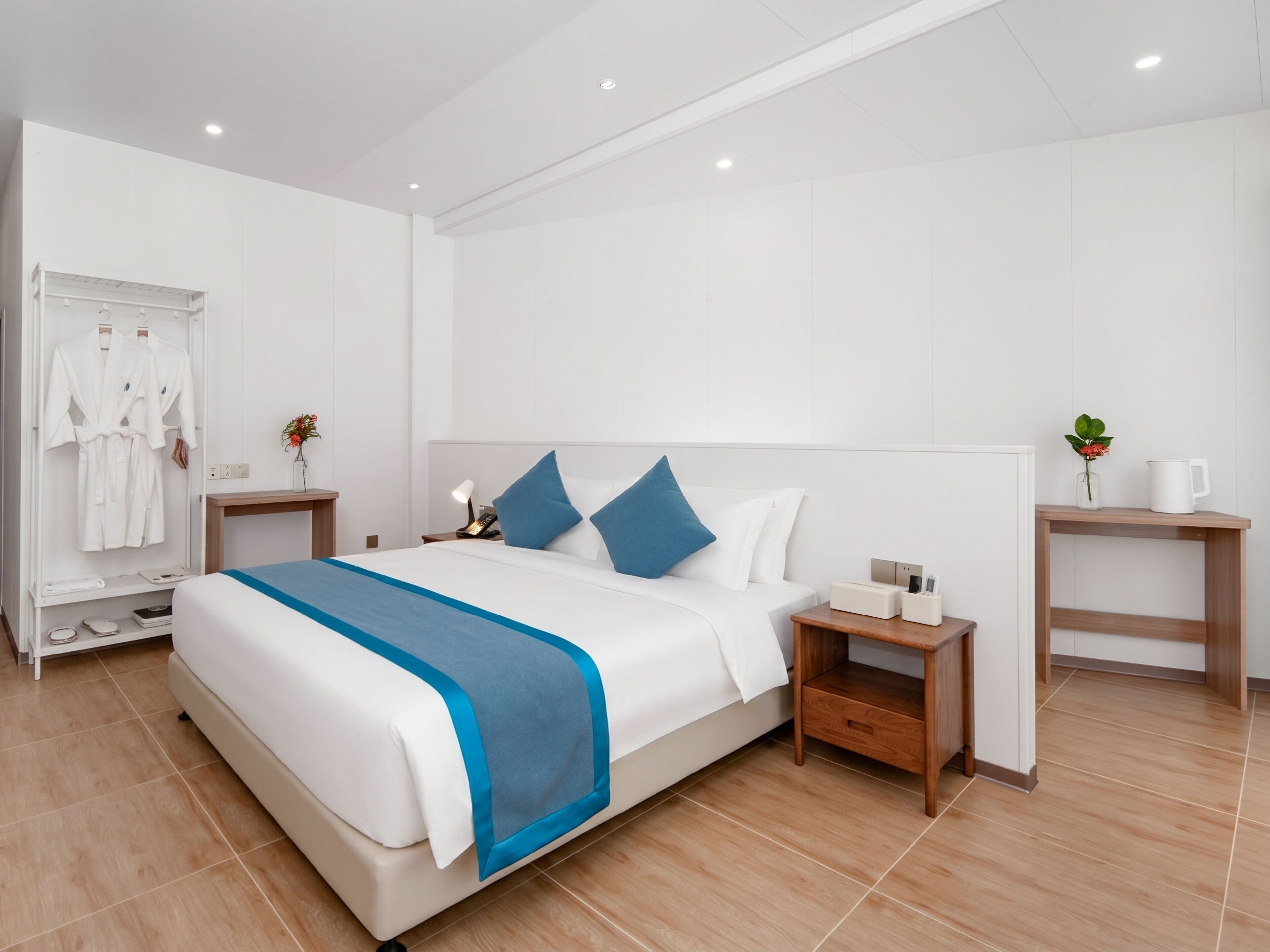 Une chambre d’hôtel moderne avec un grand lit, des tables de chevet, un porte-peignoir et une petite plante.