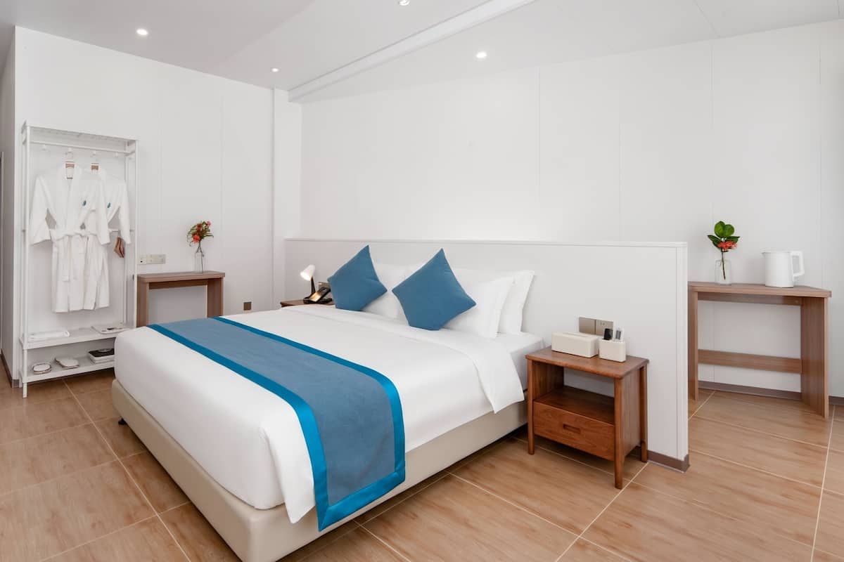 Ein modernes Hotelzimmer mit einem großen Bett, Nachttischen, einem Bademantelständer und einer kleinen Pflanze.