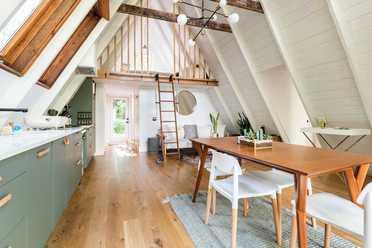 A loft-style kitchen with wooden beams, a dining area with a wooden table and chairs, and a view of the outdoors.