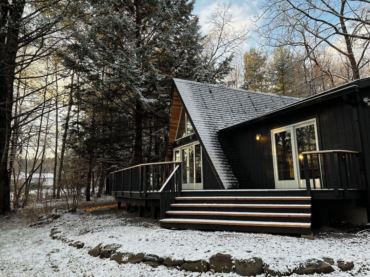 A cabin with a steep roof, wooden exterior, and a staircase leading to the entrance.
