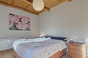A bedroom with a bed, bedside table, lamp, radiator, and a wall with a floral painting. - Casa Rural Ucedo: Peace and Nature with Mountain Views (Ucedo)