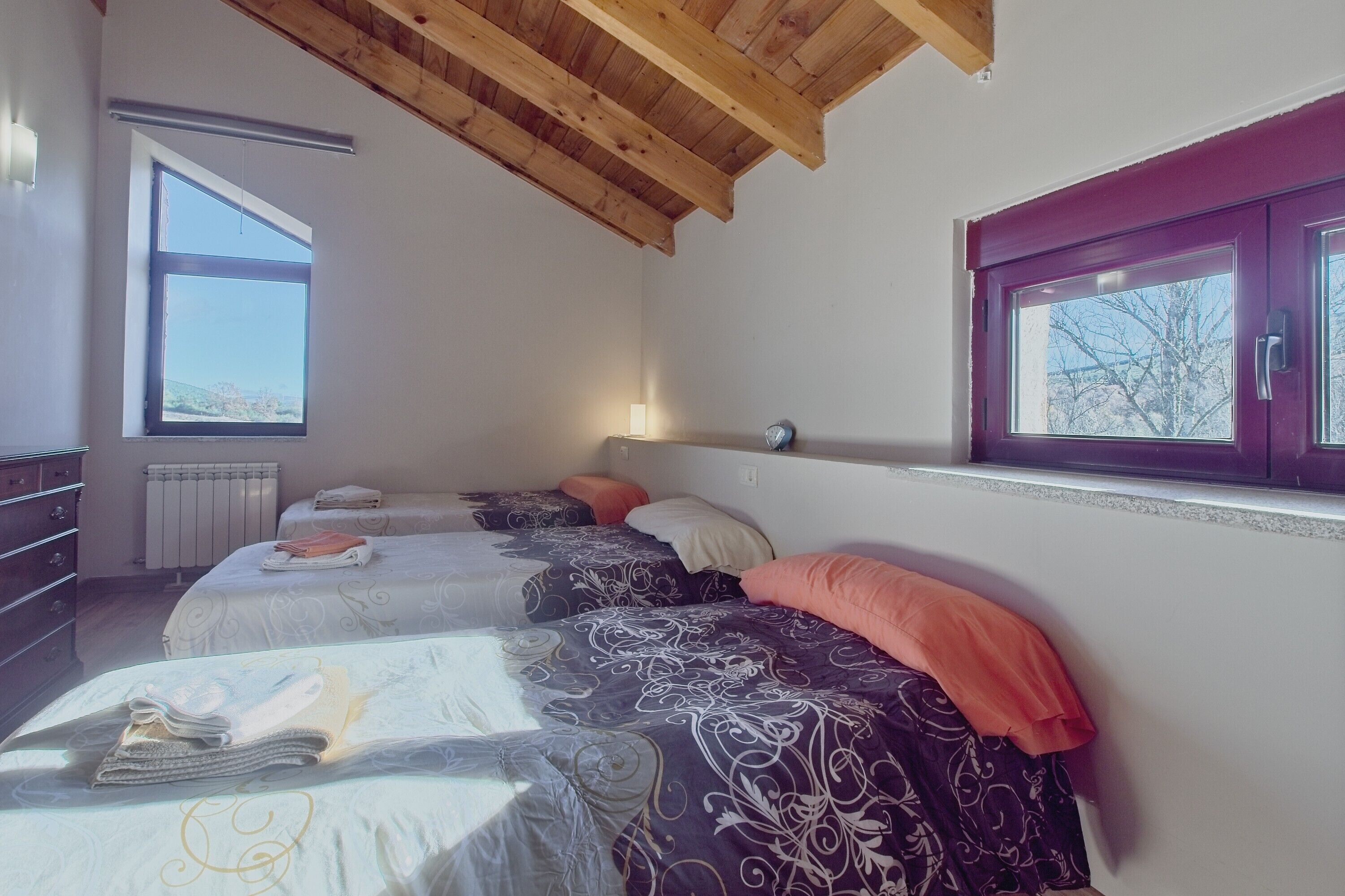 Camera da letto con tre letti, una cassettiera, una finestra vista e soffitto in legno.
