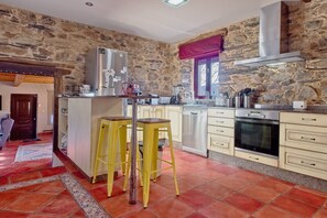 A kitchen with stone walls, a stainless steel refrigerator, a built-in oven, and yellow stools. - Casa Rural Ucedo: Peace and Nature with Mountain Views (Ucedo)