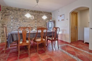 A dining area with a stone wall, wooden chairs, a table, and a chandelier. - Casa Rural Ucedo: Peace and Nature with Mountain Views (Ucedo)