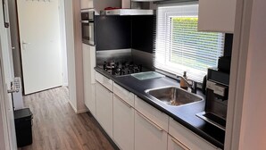 Una cocina moderna con armarios blancos, encimera negra, electrodomésticos de acero inoxidable y una ventana con persianas.