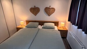 Una cama doble con dos mesitas de noche, cada una con una lámpara, en una habitación con cabecera de madera y dos decoraciones de corazón en la pared.