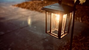 Un farol con una fuente de luz, estructura metálica y asa curvada.