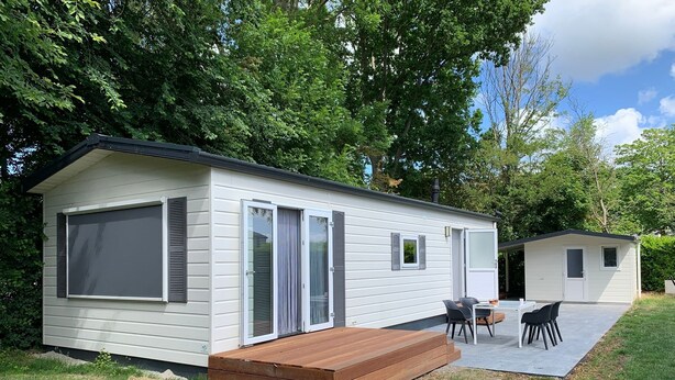 Una casa móvil de un piso con un patio, una pequeña terraza y una mesa con sillas.
