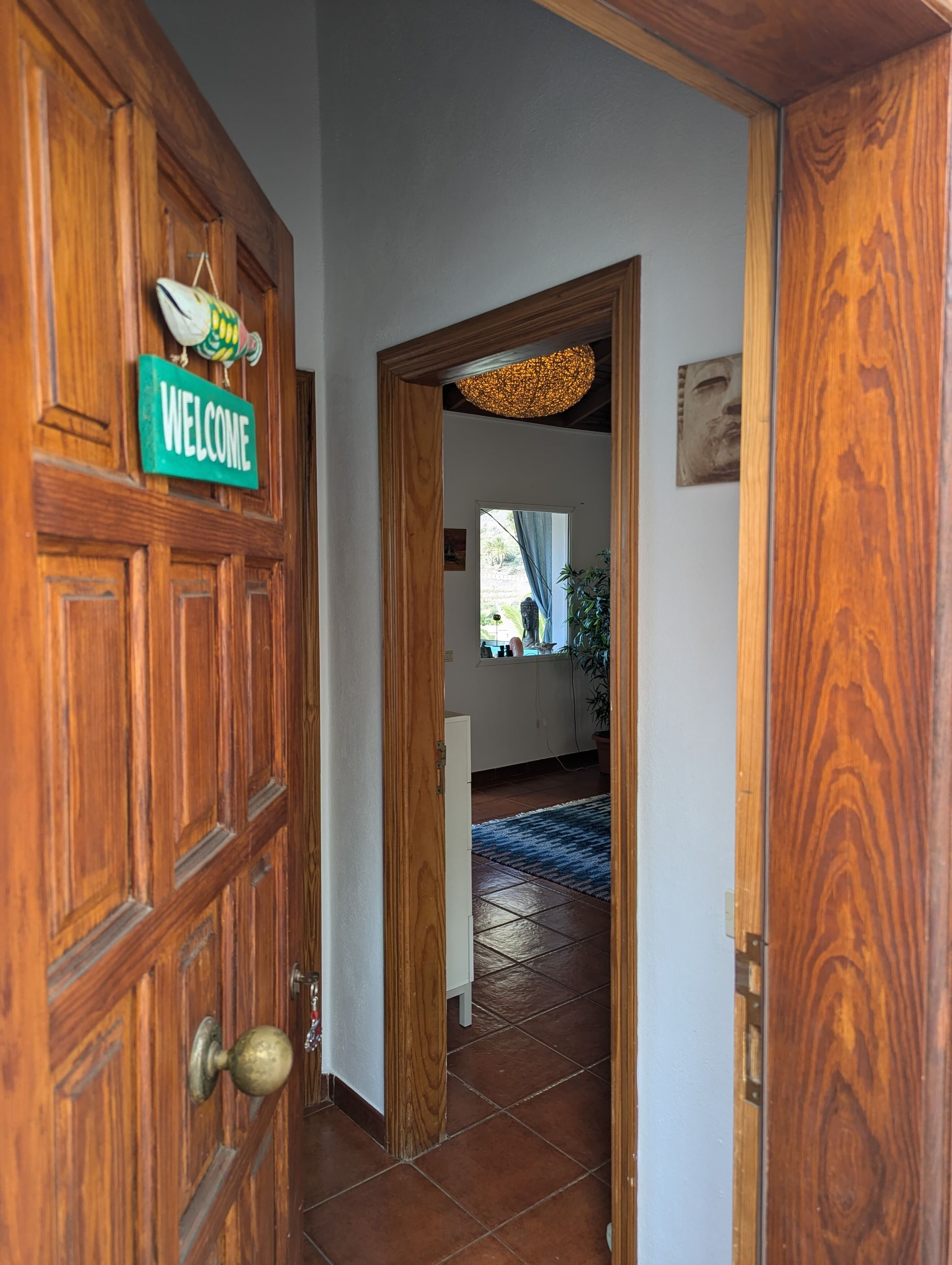 A wooden door with a 'WELCOME' sign, a tiled floor, and a hallway leading to a room with a blue carpet.