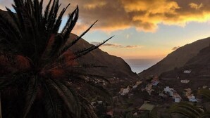 Vista panoràmica d'una població costanera amb una palmera destacada en primer terme, una vall i un cel al capvespre.