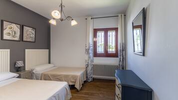 Un dormitorio con dos camas, un aparador, un radiador, una ventana con cortinas y obras de arte colgadas en la pared.