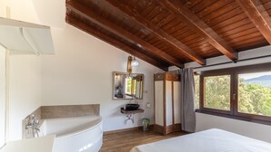Un dormitorio con una cama grande, un baño con bañera, lavamanos y ventana con vistas al exterior.