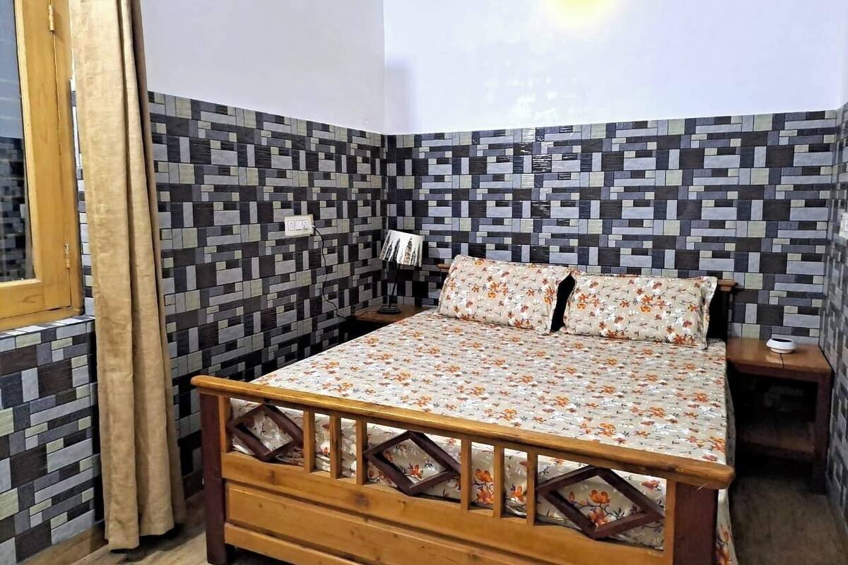 A bedroom with a wooden bed, patterned walls, a nightstand, and a window with curtains.
