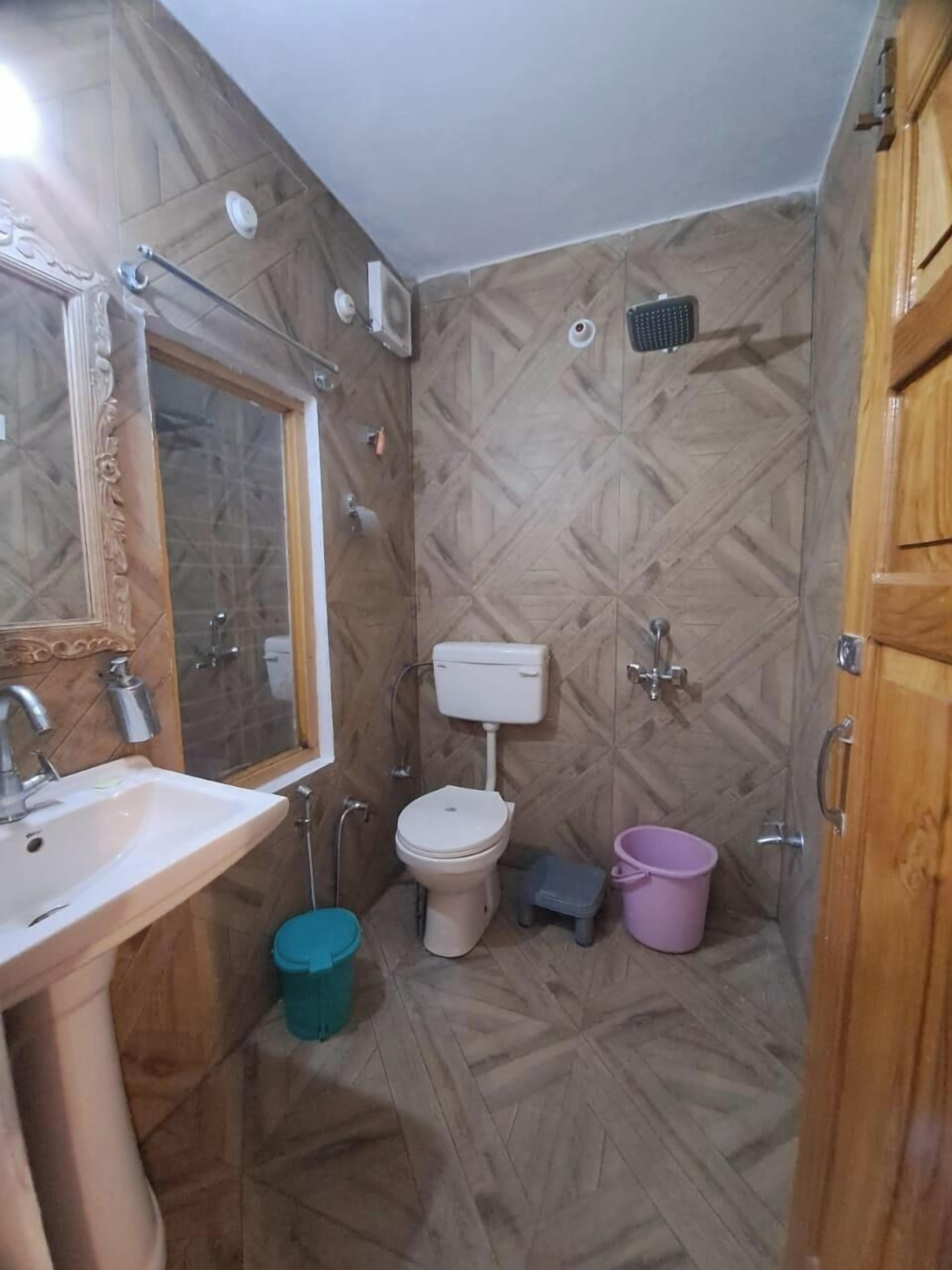 A bathroom with a wooden floor, a white sink, a toilet, and a mirror.