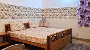 Een slaapkamer met een houten bed, een bureau, een stoel, een plafondventilator en behang met een patroon.