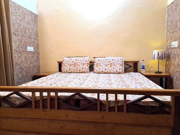 Une chambre avec un lit en bois, une literie à motifs floraux et une petite table de chevet avec une lampe.
