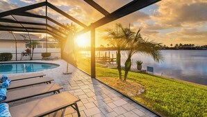 A poolside area with lounge chairs, a pool, and a view of a lake during sunset. - Intervillas Florida - Villa Bluesky at the Lake (Cape Coral)