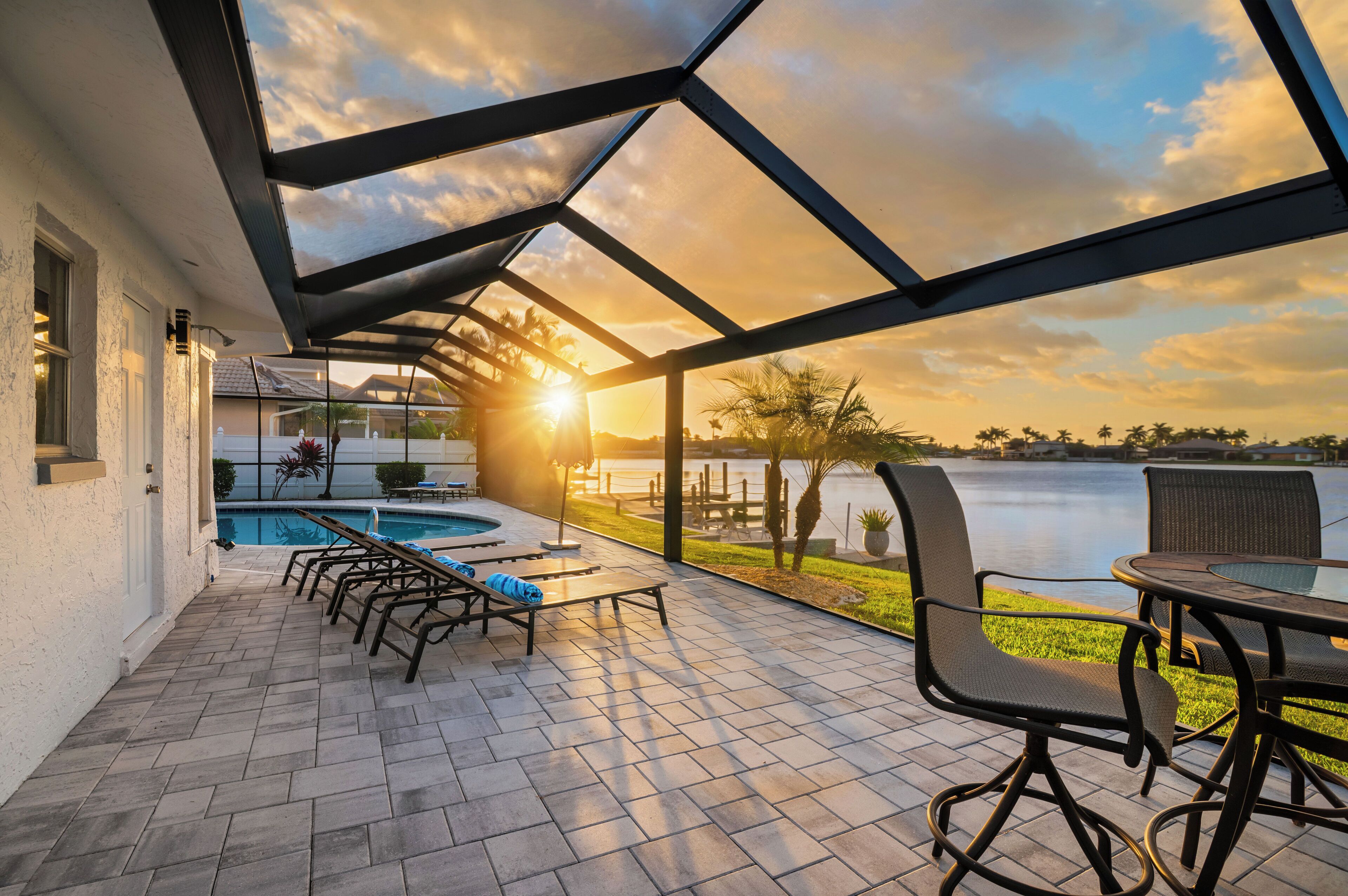 Une terrasse couverte avec une piscine, du mobilier d ’extérieur et une vue sur un lac au coucher du soleil.