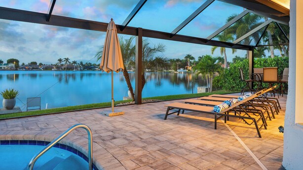 A pool area with lounge chairs and a view of a lake. - Intervillas Florida - Villa Bluesky at the Lake (Cape Coral)