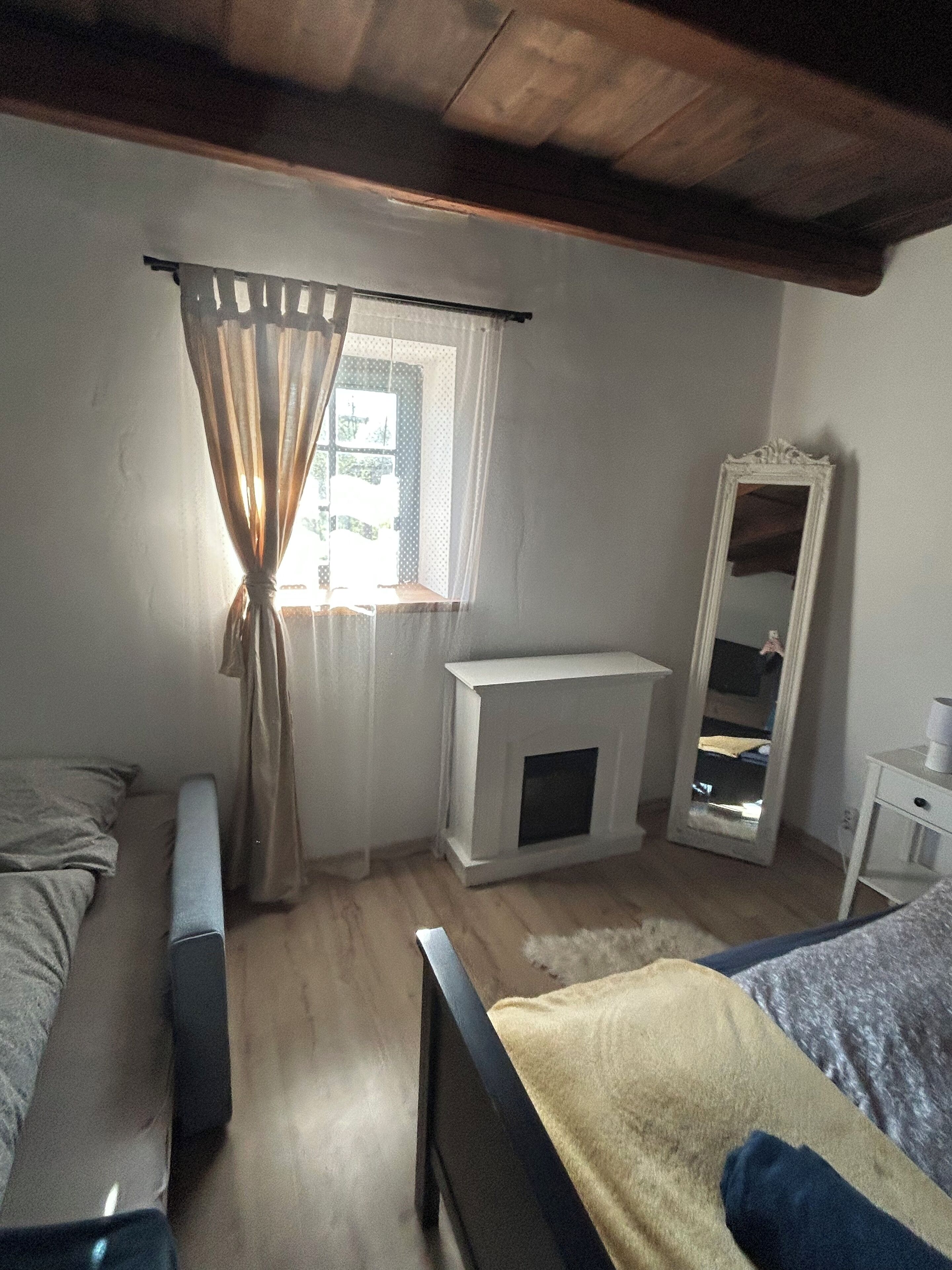A bedroom with a bed, a bedside table, a mirror, a window with curtains, and a fireplace.