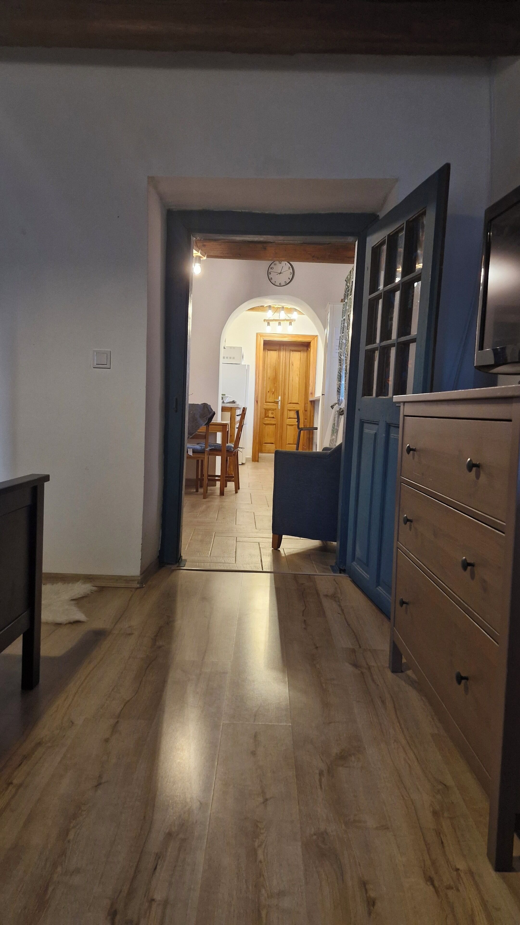 Un couloir avec un plancher en bois, un coin repas avec une table et des chaises, et un buffet bleu avec des tiroirs.