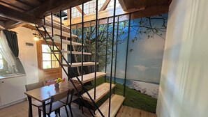 Un interior moderno con una escalera de madera, una zona de comedor con mesa y sillas, y un mural con una escena costera.