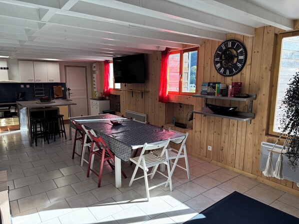 A spacious kitchen with a dining area, wooden walls, a large clock, and a TV.