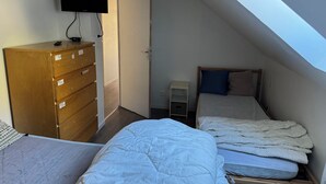 Een studentenkamer met een houten dressoir, een bed met witte beddengoed en een aan de muur bevestigde televisie.