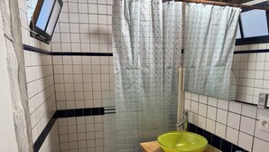 Een badkamer met een houten wastafel, een geel wasbakje, een spiegel, een douchegordijn en een raam.