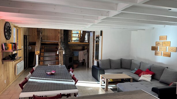 Een gezellige woonkamer met een eethoek, houten wanden, een open haard en een bank.
